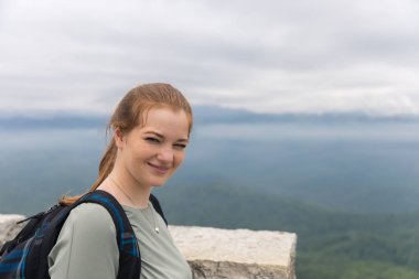 Sırt çantası kızla dağın tepesinde duran ve gülümseyen