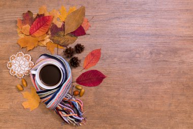 Kurumuş akçaağaç yaprakları ve zencefilli ekmekle ahşap masada sıcak eşarp içinde kahveyi kucakla.