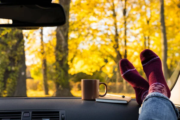 Autumn car trip. Woman feet in warm wool socks and cup of tea in the car