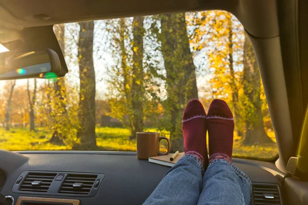 Autumn car trip. Woman feet in warm wool socks and cup of tea in the car