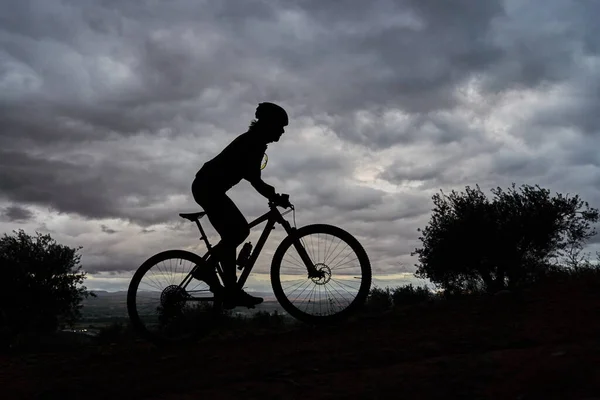 silhouette of a mountain biker climbing with clouds in the background