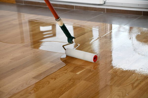 Lacquering wood floors. Worker uses a roller to coating floors. Varnishing lacquering parquet floor by paint roller - second layer. Home renovation parquet