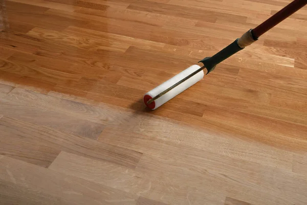 Lacquering wood floors. Worker uses a roller to coating floors. Varnishing lacquering parquet floor by paint roller - second layer. Home renovation parquet