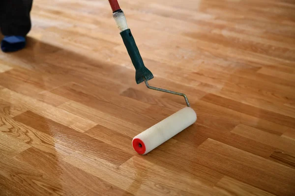 Lacquering wood floors. Worker uses a roller to coating floors. Varnishing lacquering parquet floor by paint roller - second layer. Home renovation parquet