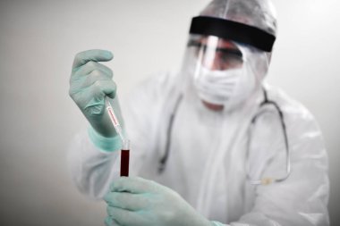 Solunum maskesi takan ve Coronavirus Covid-19 kan örneğini elinde tutan bir doktor. Bilim insanları Covid-19 ya da Corona virüsünü laboratuvar ya da hastanede hastalıkları araştırmak ve tedavi etmek için bilim tüplerini kullanarak test ediyorlar. Tıbbi tedavi kavramları
