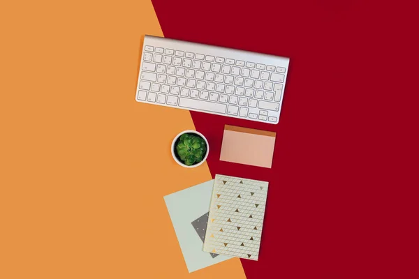 Flat lay workspace desk with keyboard, flower pot and notebooks with copy space background, minimal creative styled red and orange
