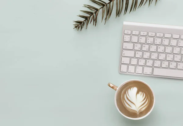 Minimalist Flat Lay Hipster Desktop With keyboard, coffee and green tropical leaves