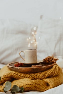 Kahve fincanı bir ahşap tepsi ve arka plan bokeh bulanıklık ışıkları ile sıcak kazak yerleştirilir. Sabah yatakta. Kopya alanı ile natürmort kompozisyon 