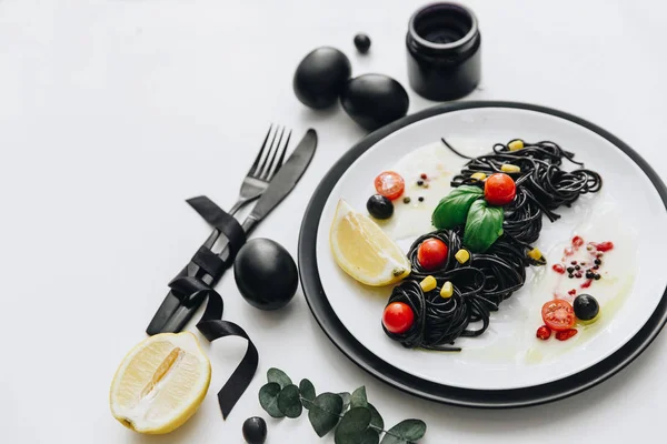 Siyah spagetti Bazilikası'nın ve domates masada. Siyah Paskalya yumurtaları. 