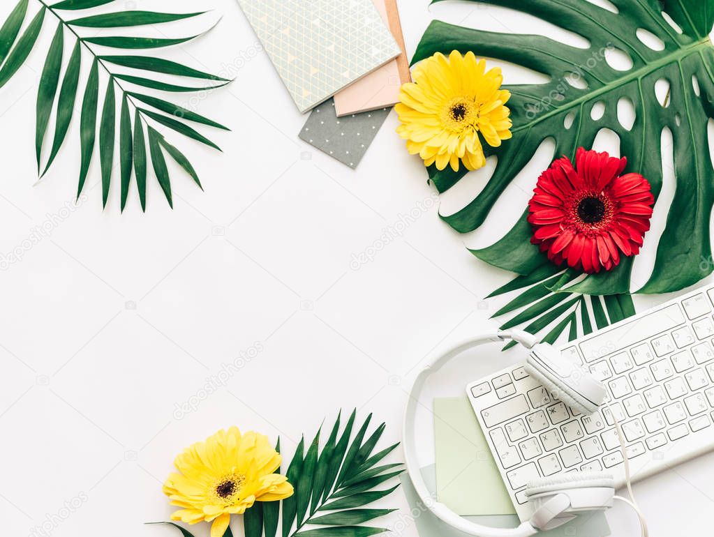 Summer concept, flat lay tropical leaves with headphones, keyboard, and flowers.