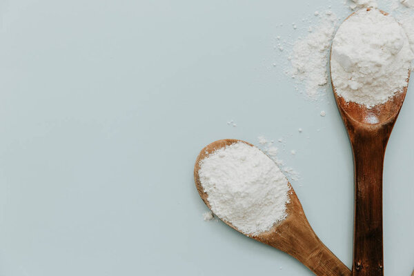 Wooden spoon with flour on pastel background. Top view, flat lay 