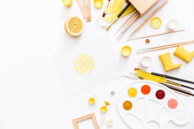 Sanatçı çalışma alanı boyalar, boya fırçaları, beyaz zemin üzerine sarı tüyleri ile