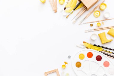 Sanatçı çalışma alanı boyalar, boya fırçaları, beyaz zemin üzerine sarı tüyleri ile