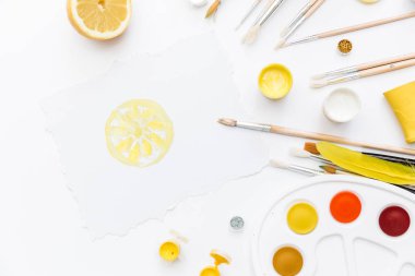 Sanatçı çalışma alanı boyalar, boya fırçaları, beyaz zemin üzerine sarı tüyleri ile