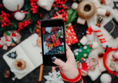 Bir kadının eli, Noel kompozisyonunun mobil bir fotoğrafını çekiyor. Çekim sırasında mobil kameralı akıllı telefon. Üst görünüm 
