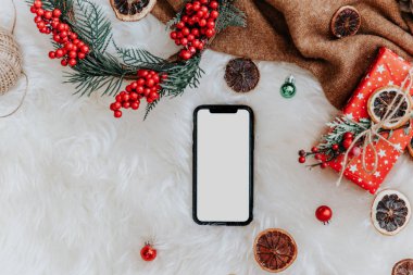 Noel şakası, Noel süslemeleri ile kürklü beyaz battaniyenin üzerinde boş ekranlı akıllı telefon 