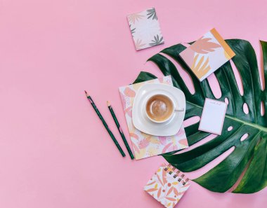 Monstera yapraklı bir fincan kahve pembe arka planda tropikal yapraklar, üst manzara, düz yatış, kopyalama alanı 