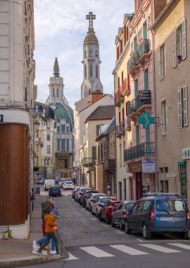Vichy, Auvergne / Fransa - 26 Kasım 2019: Önden karşıya geçen yayalar ve arka planda Art Deco tarzı Saint-Blaise Kilisesi tarzı bir sokak perspektifi.