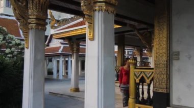 Kırmızı elbiseli genç bir kadın Bangkok, Tayland 'da bir Budist tapınağında yürüyor. Kamera solda dolanıyor..