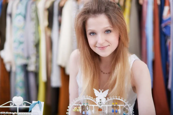 Χαμογελώντας νεαρή γυναίκα κρατώντας φόρεμα και χαμογελώντας ενώ στέκεται στο κατάστημα ρούχων — Φωτογραφία Αρχείου