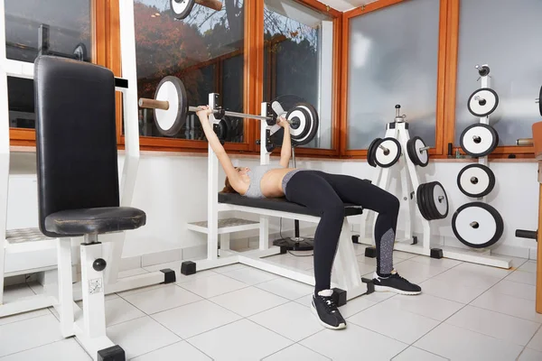 Mujer en forma joven haciendo ejercicio con barra de pesas en el banco en el gimnasio — Foto de Stock