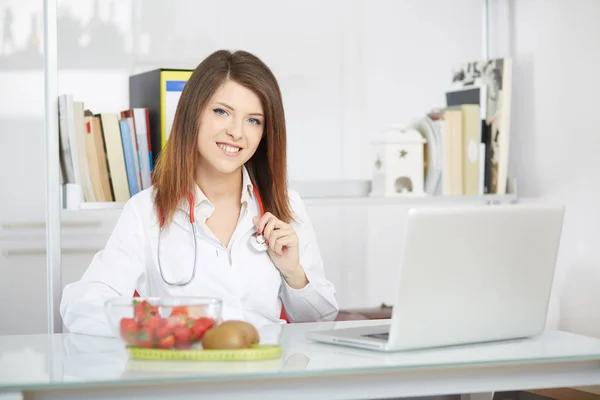 Smiling nutritionist writing medical records with fresh fruit on foreground — Stock Photo, Image