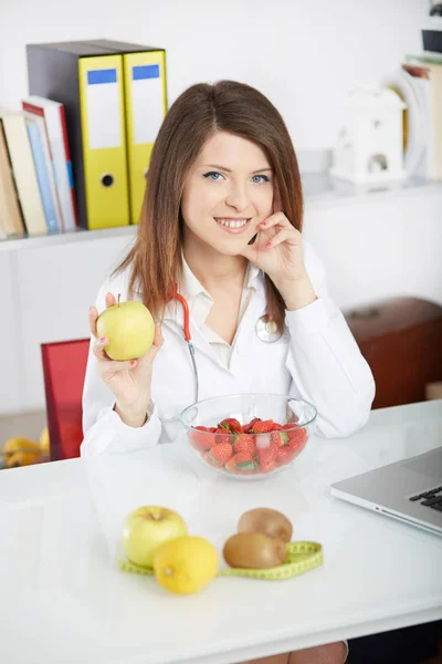 Smiling nutritionist showing apple with fresh fruit on foreground — Stock Photo, Image