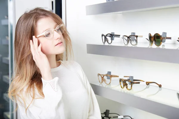 Bella, giovane donna che sceglie nuove cornici per occhiali in un negozio di ottica — Foto Stock