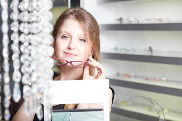 Pretty, young woman choosing new glasses frames in an optician store — Stock Photo, Image