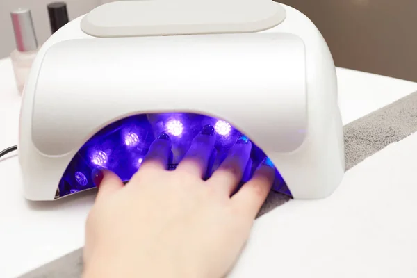 Primo piano di una lampada UV con una mano femminile all'interno fissare lo smalto gel presso il salone di bellezza — Foto Stock