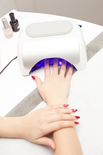 Närbild av en UV-lampa med en kvinnlig hand inuti fastställande gel nagellack på skönhetssalongen — Stockfoto