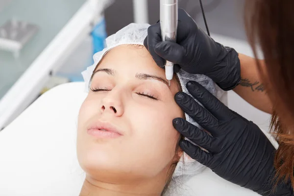 Schöne junge Frau, die sich tätowieren lässt. Tätowierer macht Augenbrauen-Make-up — Stockfoto