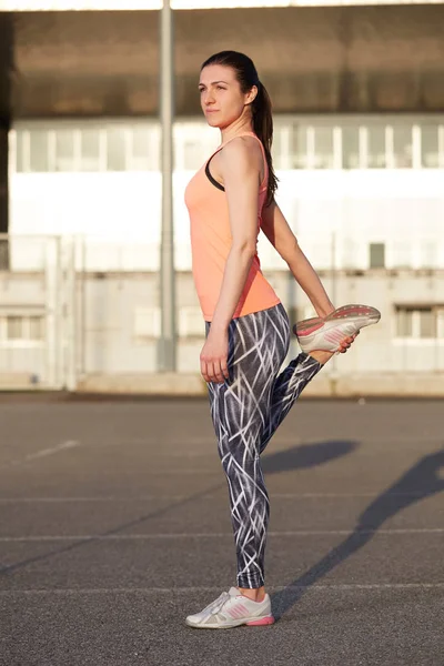 Mujer joven en forma estirando su pierna antes de una carrera en las calles de la ciudad — Foto de Stock