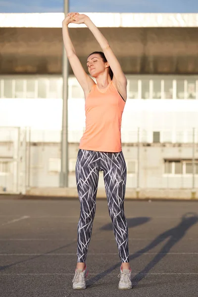 Mujer joven en forma estirando su pierna antes de una carrera en las calles de la ciudad — Foto de Stock