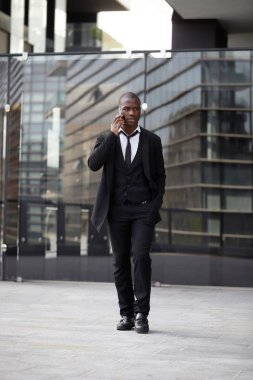 Şehirde cep telefonuyla konuşan kendinden emin genç bir işadamının tam boy portresi.