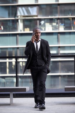 Şehirde cep telefonuyla konuşan kendinden emin genç bir işadamının tam boy portresi.