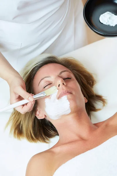 Beautiful young woman having a facial cosmetic mask at spa salon