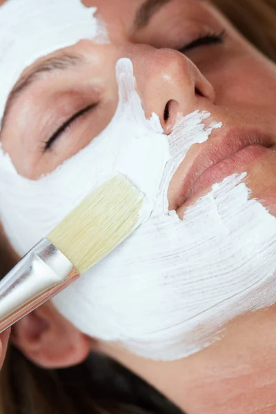 Beautiful young woman having a facial cosmetic mask at spa salon