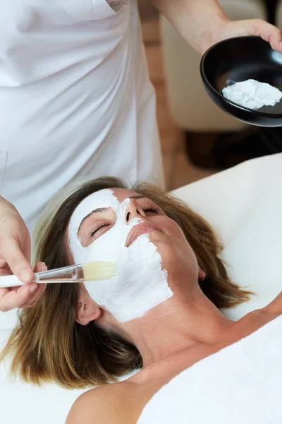 Beautiful young woman having a facial cosmetic mask at spa salon