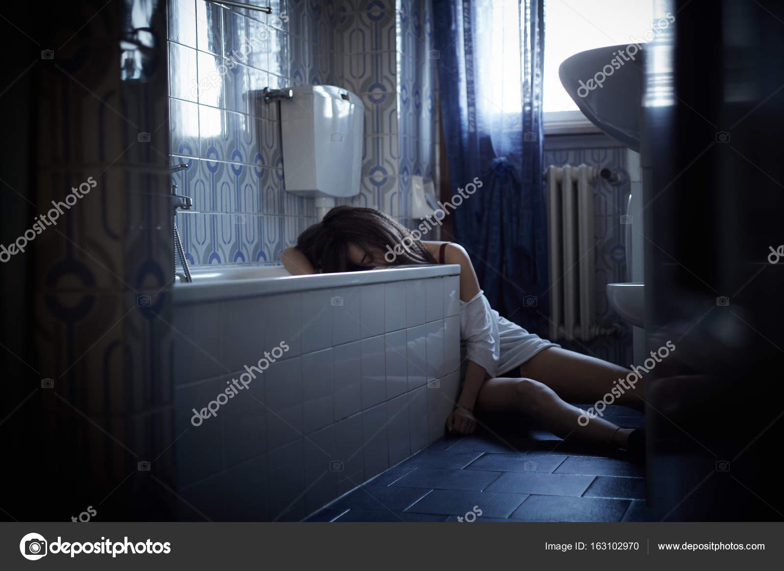 Girl addict unconscious sitting on the bathroom's floor Stock Photo by