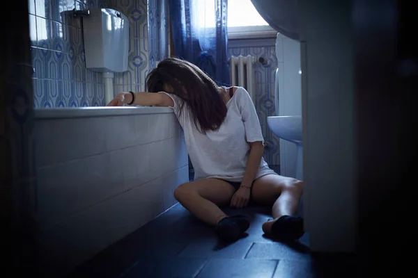 Chica adicta inconsciente sentado en el suelo del baño —  Fotos de Stock