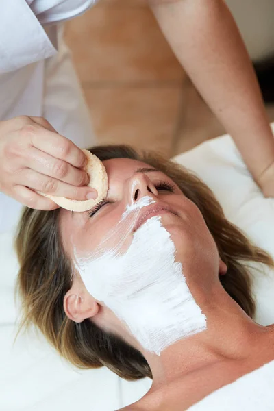 Beautiful woman with clear skin getting facial mask at salon