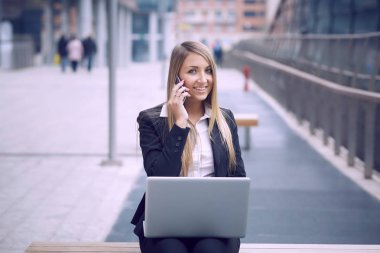 dizüstü bilgisayar kullanarak ve kentsel çevre için mobil konuşmak güzel iş kadını