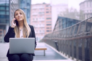 dizüstü bilgisayar kullanarak ve kentsel çevre için mobil konuşmak güzel iş kadını