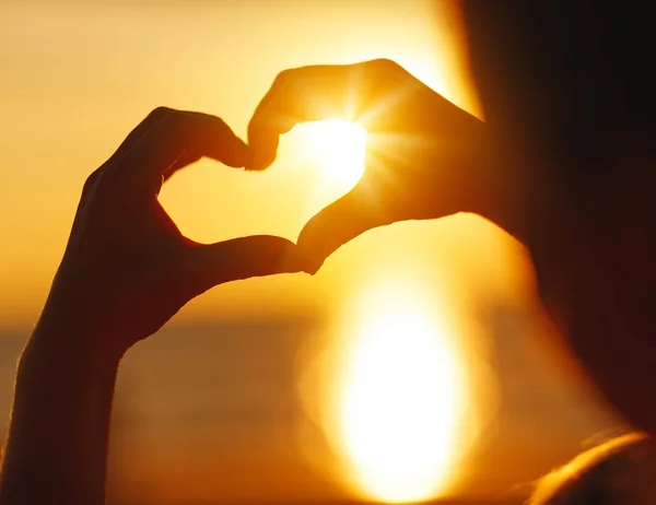 Mani a forma di cuore al tramonto sulla spiaggia — Foto Stock