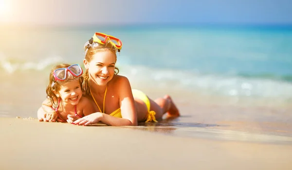 Счастливая семья мать и дочь в масках на пляже в сумме — стоковое фото