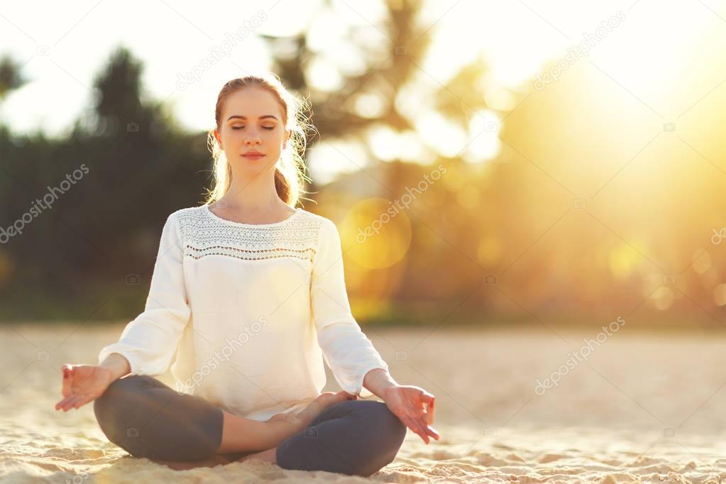 woman practices yoga and meditates in lotus position on beach