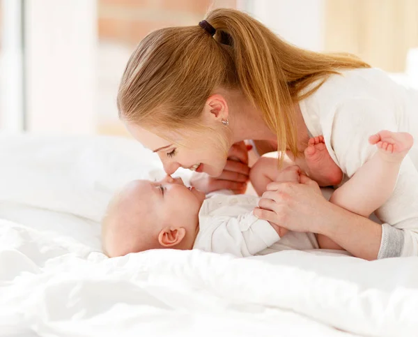 Família feliz mãe e bebê brincando, abraçando na cama — Fotografia de Stock