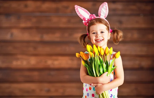 Feliz risueño niña en conejito orejas con amarillo tulipanes en — Foto de Stock