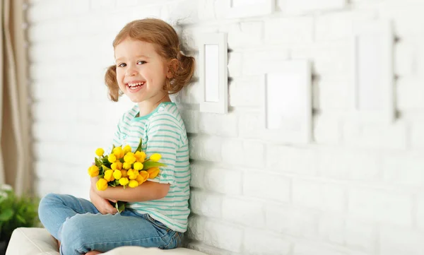 Glücklich lachendes Kind Mädchen mit gelben Tulpen zu Hause — Stockfoto